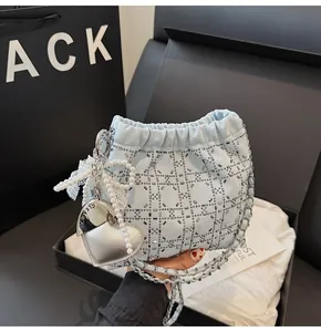 Detalle de bolso tipo cubo azul claro con pedrería, colgante de corazón y cadena