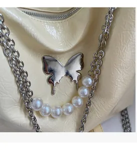 Detail of cream tote bag featuring silver butterfly hardware, pearls, and crinkled leather