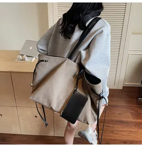 Close-up of large khaki canvas tote bag with slim black leather straps and side drawstring detail