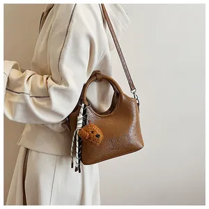 Detailansicht der braunen Leder-Eimertasche mit weichem Teddy-Anhänger und Trageriemen