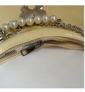 Detail of smooth metal zipper and pearl chain with silver butterfly charm on cream tote bag