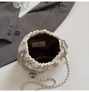 Vista detallada del bolso saco con pedrería en blanco crema, cadena y amplio compartimento