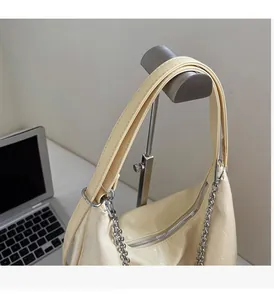 Detail of cream hobo bag with subtle texture, silver chain and wide strap on metal stand