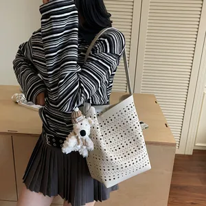 White hollow-out bucket bag with plush dog charm shown as a stylish shoulder bag for women