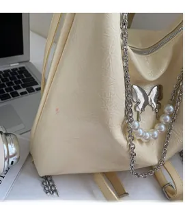 Detail of cream tote bag featuring silver butterfly charm and faux pearl chain strap