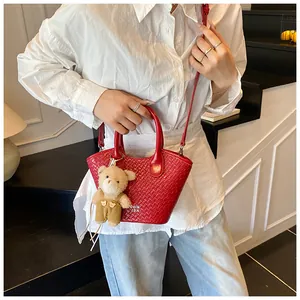 Detail view of red woven bucket bag with cute bear charm and white logo lettering