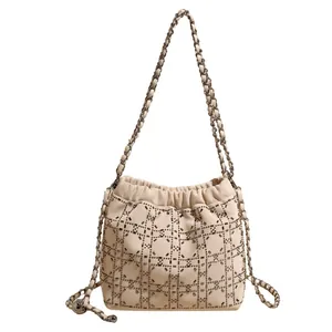 Elegante bolso tipo cubo crema con pedrería y tachuelas metálicas en fondo blanco