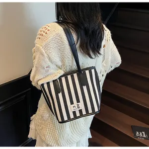 Gros plan du sac cabas rayé noir et blanc avec lanières en cuir et logo brodé