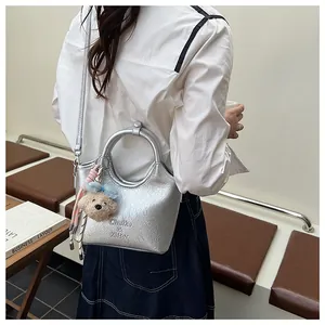 Detailansicht der silbernen Metallic-Handtasche mit Plüschbär-Anhänger an weißem Hemd
