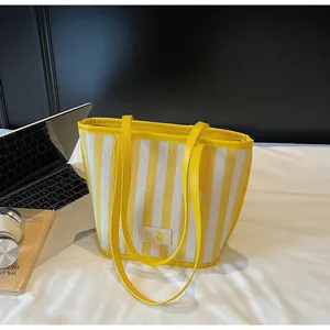 Détail du sac cabas en toile à rayures jaunes et blanches avec anses en cuir et ordinateur