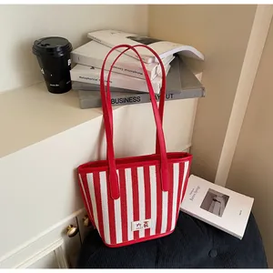 Détail du sac cabas à rayures rouges et blanches avec anses en cuir rouge et étiquette logo