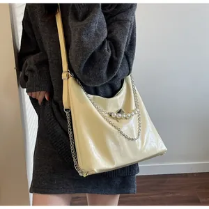 Model wearing a large light yellow faux leather hobo tote with chain and pearl charms