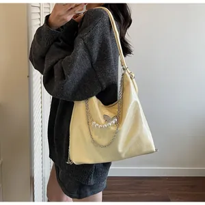 Close-up of cream yellow tote bag with silver butterfly clasp and pearl chain detail