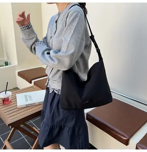 Close-up of a black minimalist tote bag with metal logo detail on a female model