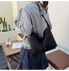 Detail of minimalist black hobo bag with adjustable strap and metal logo in outdoor setting