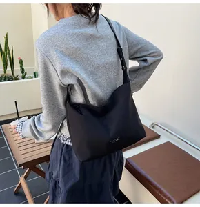 Minimalist black nylon hobo bag shown on a model in a sunlit outdoor setting