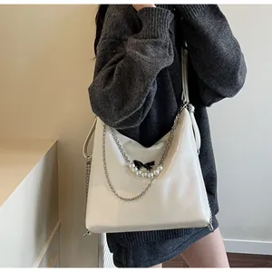 Close-up of white glossy tote with black bow, pearl charms and silver chain detail