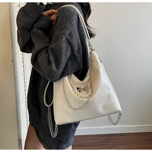 Detail of a shiny off-white tote bag with a metal butterfly buckle and pearl pendant