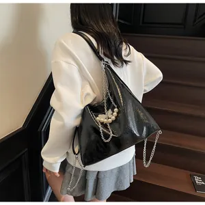 Detail of black glossy crinkled leather tote bag with silver butterfly chain and pearl charm