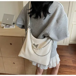 Detail shot of a white tote bag with metallic butterfly charm and pearl chain accent