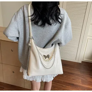 Detail of cream PU tote bag featuring a silver butterfly charm and pearl chain accent