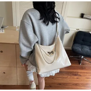 Detail of beige hobo bag with glossy finish and silver butterfly chain ornament