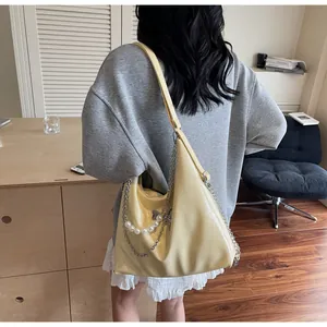 Detail of light yellow Hobo bag with glossy leather, silver chain and pearl ornaments