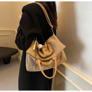 Détail d'un sac cabas en daim kaki avec un pendentif baseball et une large bandoulière