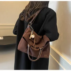 Détail d'un grand sac cabas en daim marron avec charm de baseball et bandoulière en cuir