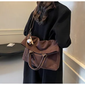 Détail du grand sac à bandoulière en daim marron avec poignées en cuir et breloque baseball