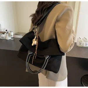 Détail du grand sac cabas noir en daim avec pendentif baseball sur un blazer beige