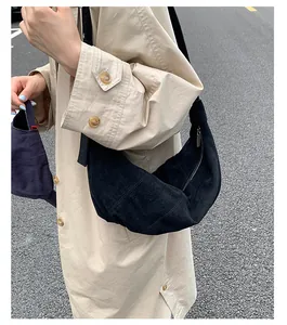 Détail d'un sac demi-lune noir en daim porté avec un manteau beige dans un décor de rue