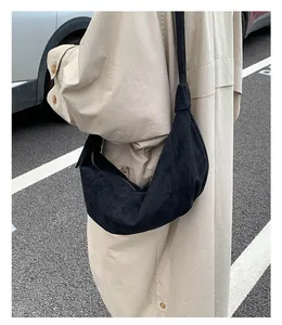 Détail d'un sac demi-lune en daim noir porté avec un manteau beige élégant