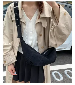 Détail du sac croissant en daim noir avec bandoulière large et œillets métalliques