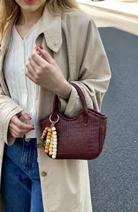 Close-up of woven burgundy bucket bag featuring a decorative wooden bead tassel detail
