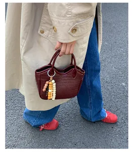 Detail of burgundy woven bucket bag with colorful wooden bead charm in a street setting
