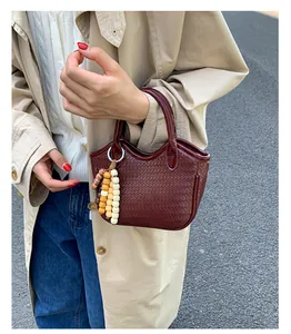 Close-up of a dark red woven bucket bag with beaded tassel detail and crossbody style