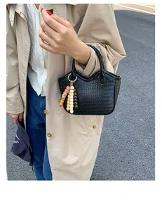 Detail of black woven bucket bag with vintage bead charm held by a model in beige coat