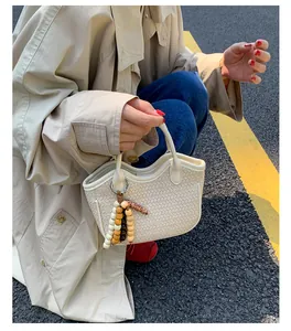 Detail of cream woven bucket bag with beaded tassel charm in a street style setting