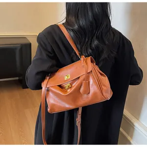 Caramel leather tote bag with double gold twist locks shown on a black blazer