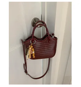 Close-up of dark red woven bucket bag with wooden bead charm hanging on a white door