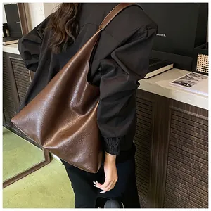Detail of a large brown textured leather tote bag with a retro minimalist shoulder strap