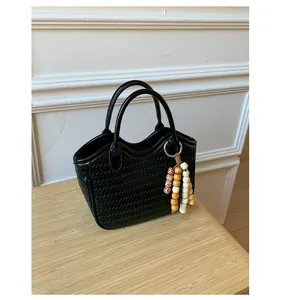 Detail view of black woven bucket bag with wood bead charm on a light wood surface