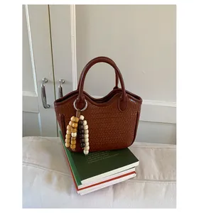 Detail of dark brown woven bucket bag featuring a beaded tassel charm on a book stack