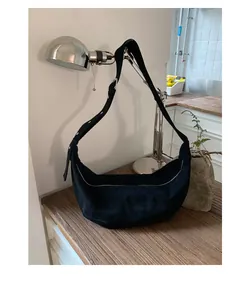 Détail du sac croissant en daim noir avec bandoulière réglable sur une table en bois