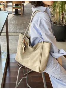 Detail of apricot matte tote bag with wooden bead charm worn by model in striped shirt