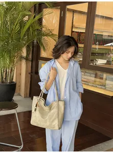 Detail of khaki tote bag with beaded pendant worn by a model in sunny cafe setting
