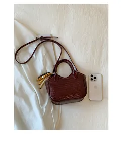Detail of woven burgundy bucket bag featuring a beaded tassel and shoulder strap