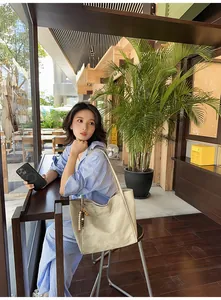 Detail of beige suede tote bag with wooden bead charm in a casual outdoor setting