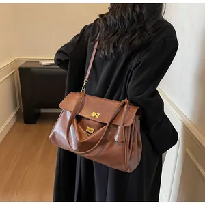 Detail of a brown leather tote bag with gold metal twist locks shown on a black coat